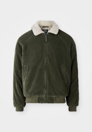 Chaqueta de pana verde con un cuello de piel sintética color crema, cremallera frontal y puños y dobladillo acanalados. Presenta dos bolsillos laterales.