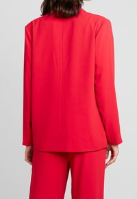 Roter Blazer mit geradem Schnitt, langen Ärmeln und ohne sichtbare Verschlüsse, aus einem glatten Stoff gefertigt. Verfügt über eine einfache Rückennaht als Detail.