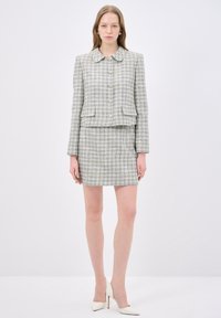 Tweed kostymset som innehåller en kragad jacka med knäppning och en åtsittande kjol; färgerna inkluderar ljusblå, beige och vit.