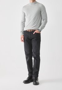 Grau gestrickter Pullover mit Stehkragen, kombiniert mit dunklen Denim-Jeans und schwarzen Schnürstiefeln. Mit einem braunen Ledergürtel und einer Armbanduhr.