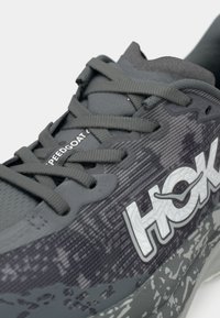 Shoe de corrida cinza com parte superior em malha texturizada, atacadores planos e logotipo impresso. Apresenta uma entressola padronizada e um salto ligeiramente elevado.