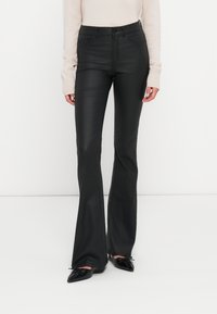 Crne široke traperice glatke teksture, visokog struka, s kontrastnim šavovima i prednjim džepovima. Uparen s svijetlosmešavom majicom.