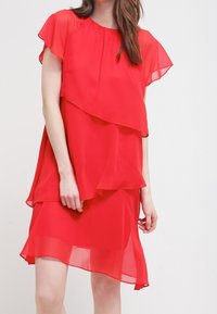 Robe en chiffon rouge avec un design à couches, des manches courtes et un ourlet asymétrique. Tissu léger avec une texture fluide.