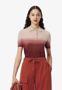 Polo à manches courtes dans un dégradé de rose clair à rouge profond, avec un col, une patte de boutonnage à trois boutons et un petit logo sur la poitrine.