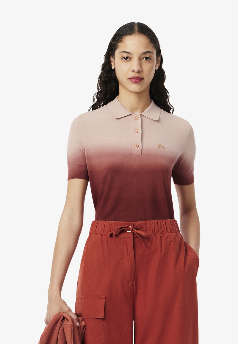 Polo à manches courtes dans un dégradé de rose clair à rouge profond, avec un col, une patte de boutonnage à trois boutons et un petit logo sur la poitrine.