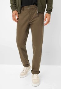 Bruine katoenen chinos met een gladde textuur, voorzien van een ritszak en opgerolde pijpen, gecombineerd met beige sneakers.