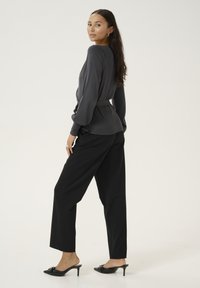 Gray long-sleeve top with belted waist, paired with black wide-leg trousers and black heeled mules on a neutral background.