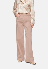 Hellbeige, weit geschnittene Baumwollhose mit Bindegürtel und Seitentaschen, kombiniert mit einer Bluse mit Blumenmuster.