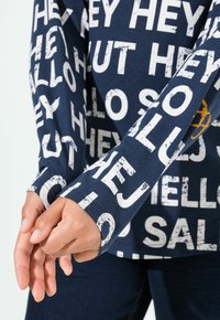 Námořnická košile s dlouhým rukávem z bavlny s velkými bílými nápisy. Rukávy jsou zakončeny viditelným šitím a mají uvolněný střih.