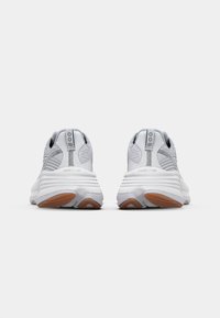 Baskets de sport blanches en tissu texturé, avec un col rembourré et une semelle en caoutchouc. Elles présentent des accents gris contrastants et des détails de logo sur le talon.