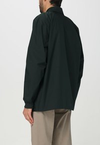 Camicia verde scuro a maniche lunghe con colletto classico, caratterizzata da una vestibilità comoda e polsini con bottone, realizzata in tessuto morbido. Dettagli minimi.