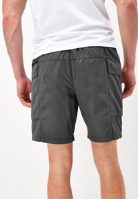 Mørkegrå cargo shorts med en glat tekstur, elastisk talje, sidelommer og syet kant, set bagfra.