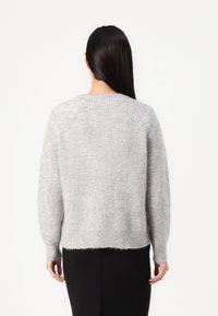 Šedý, huňatý pletený svetr s volným střihem, raglánovými rukávy a mírně zkráceným lemem. Má měkkou texturu a minimalistický design.