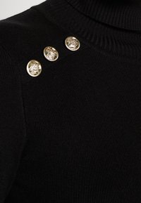 Tissu tricoté côtelé noir avec un col haut et trois boutons décoratifs dorés brillants sur l'épaule.