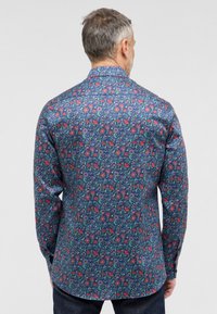 Marineblå blomsterknap-shirt med lange ærmer, der har et gentaget mønster af røde og grønne blomster på et glat stof.
