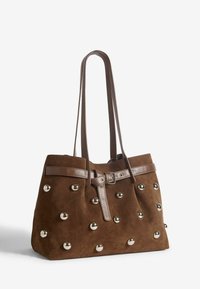 Barna velúr bevásárlótáska bőr pántokkal, ezüst színű fém szegecsekkel és csatolt öv részletekkel a tetején.