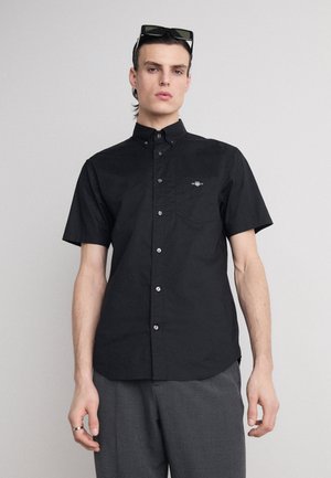 Black short-sleeve button-up shirt with a collar, featuring a small embroidered logo on the chest and silver buttons.