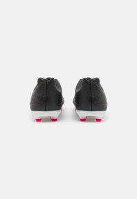 Zapatillas deportivas negras con acentos en rosa, material sintético suave, diseño de perfil bajo y suelas blancas con tachuelas rosas.