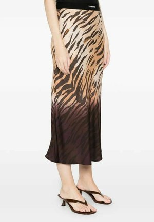 Donna che indossa una gonna di seta di lunghezza media con stampa animalier marrone e beige abbinata a sandali neri con tacco a cinturino, in piedi con le braccia rilassate.