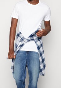 Vit t-shirt, blårutigt skjorta knuten runt midjan, ljusblå jeans. Rutig mönster med växlande mörkblå och ljusblå rutor.