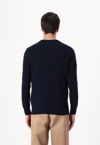 Pull marin avec col ras du cou, manches longues et texture tricot lisse. Assorti à un pantalon beige clair.