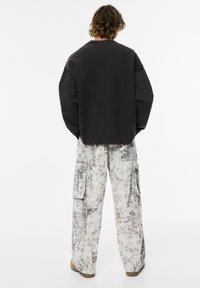 Overmaat zwart sweatshirt met verlaagde schouders, gecombineerd met cargobroek met een gewafeld, multicolor abstract patroon en zijvakken.