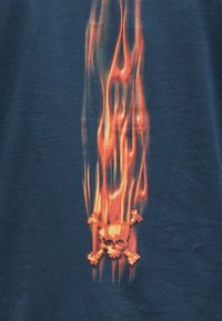 Γραφικό με φλεγόμενο κρανίο και σταυρωμένα οστά με κόκκινες και πορτοκαλί φλόγες σε σκούρο μπλε φόντο υφάσματος.