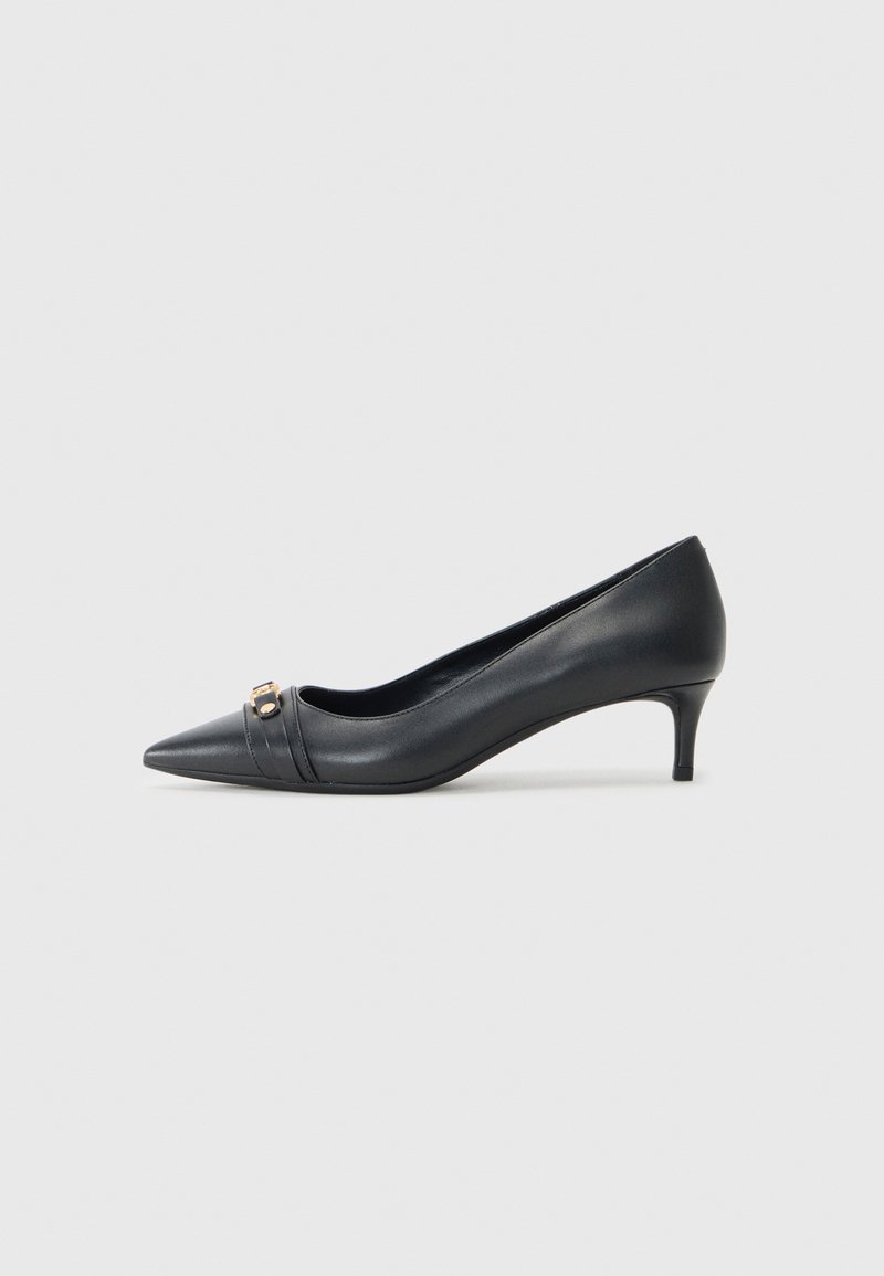 Pump nera in pelle con punta affusolata e tacco basso, caratterizzata da una tracolla testurizzata e un accento metallico sul davanti. Superficie liscia e design elegante.