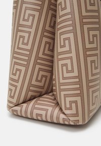 Sac à main beige avec un motif géométrique marron. Design structuré, surface texturée et coins angulaires créent un look moderne et dynamique.
