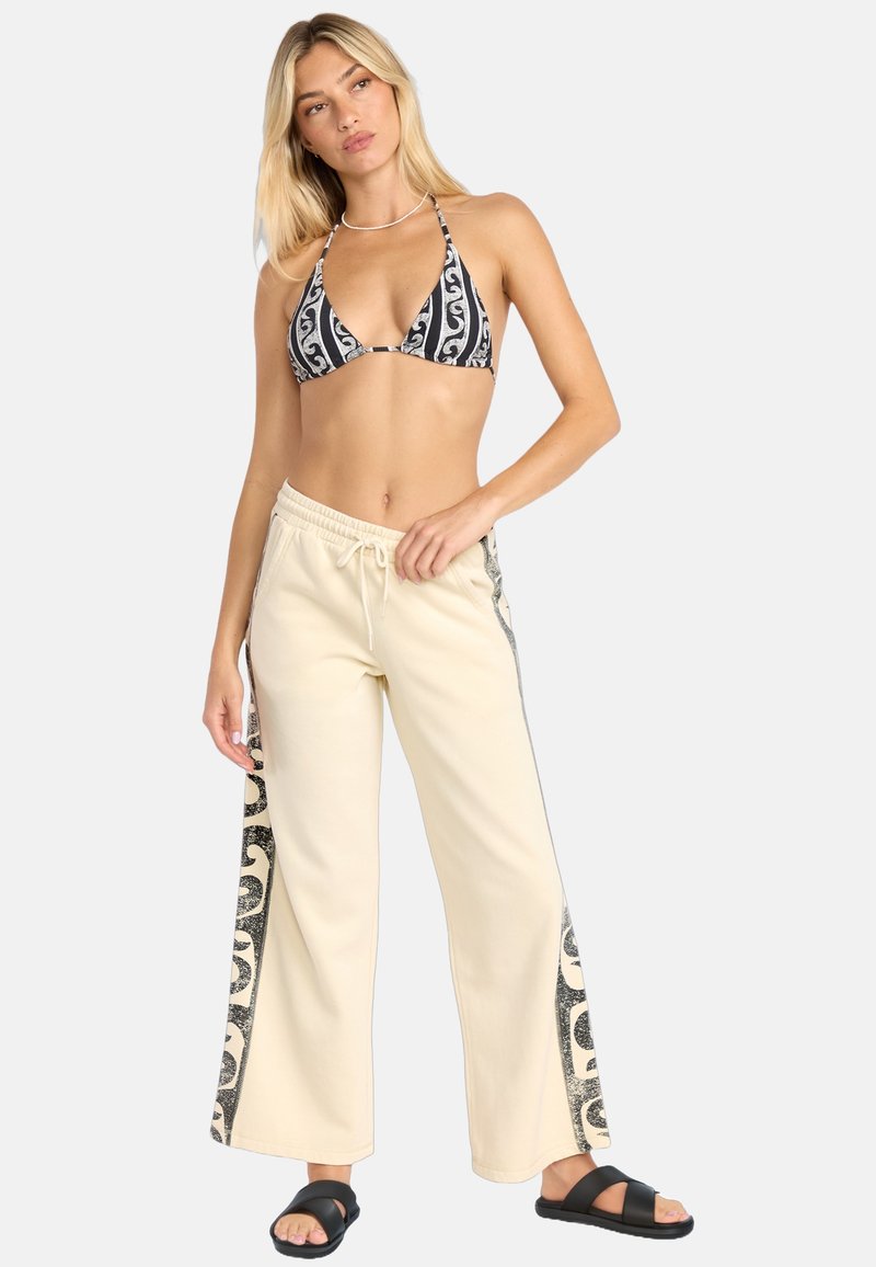 Bralette de bikini con estampado en blanco y negro, pantalones de chándal anchos color crema con detalle de patrón negro en los laterales, tejido texturizado y cintura ajustable con cordón.