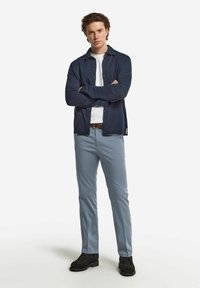 Marinblå skjorta med knappar över en vit T-shirt, matchad med ljusblå byxor och mörka skor, med klassisk passform och slät textur.