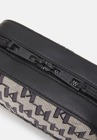 Schwarze Ledertasche mit einem gemusterten grauen Stoffboden, ausgestattet mit einem glatten Reißverschluss und geprägtem Hardware-Detail. Kompakte rechteckige Form.