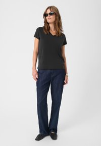 Černé tričko s výstřihem do V v kombinaci s volnými tmavě modrými džíny a černými plochými botami. Vlasy jsou vlnité a po ramena.