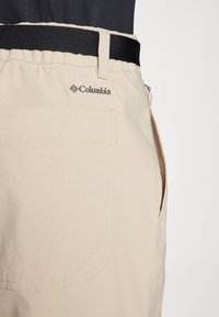 Beige lightweight shorts with an elastic waistband and a black belt. Features a side pocket and the Columbia logo on the back.
