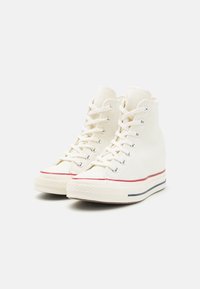 Høyhælte sneakers i off-white lerret med røde og marineblå aksenter, med snørebånd foran, gummitåhette og teksturert såle.