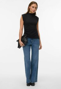 Sort ærmeløs top med høj halsudskæring, kombineret med blå jeans med vide ben. Modellen holder en sort tekstureret clutch.