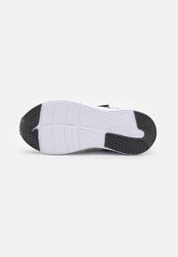 Semelle de chaussure de sport présentant un motif de bande de roulement en caoutchouc noir avec des éléments en relief, une semelle intermédiaire blanche et une surface texturée pour l'adhérence.