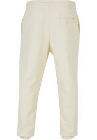 Cream-colored sweatpants made from soft material, featuring an elastic waist, side pockets, and a back pocket with a subtle stitching detail.