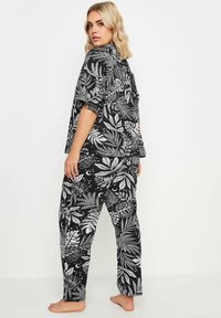 Svart pyjamasset med kortärmad topp och byxor, prydd med vita tropiska bladtryck och himmelska accenter. Mjuk tyg, avslappnad passform.