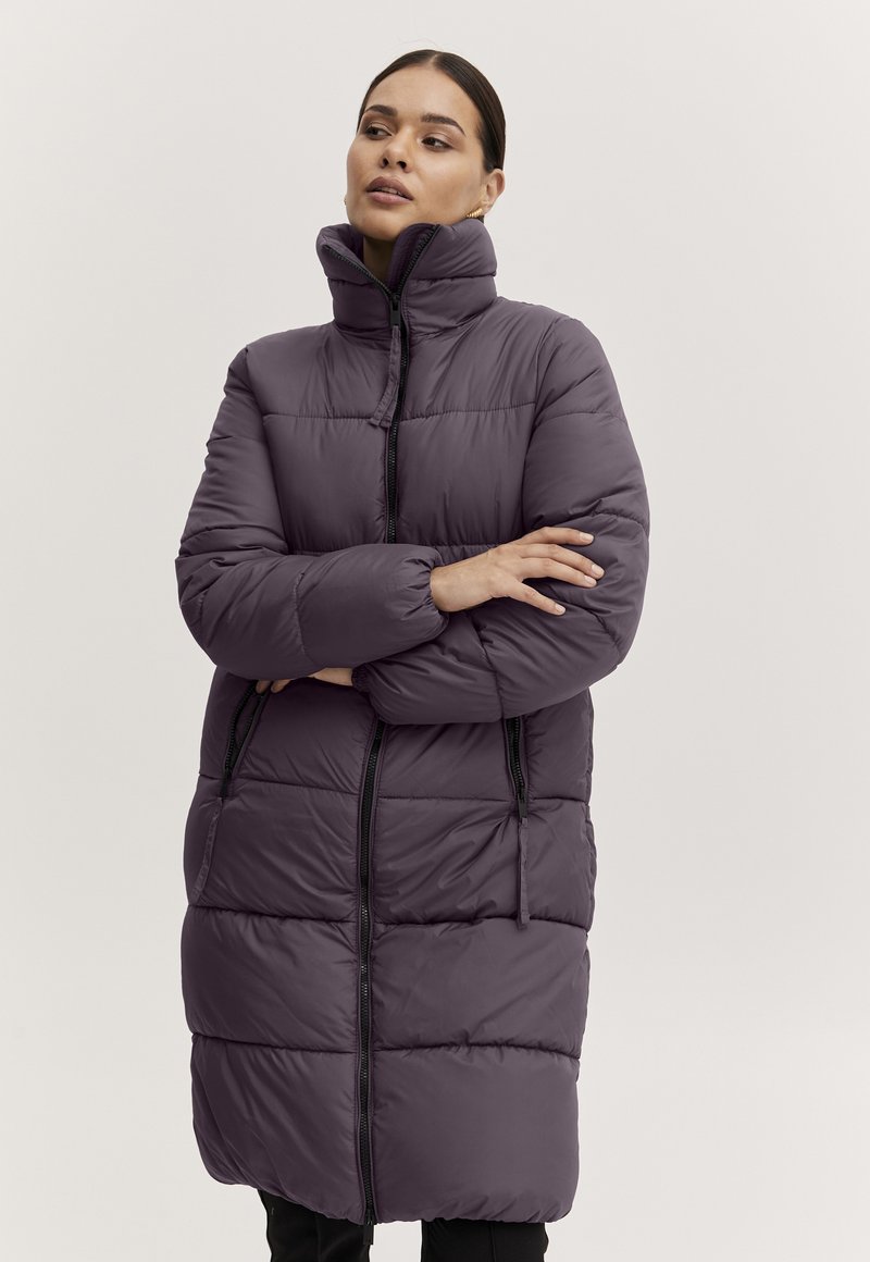 Puffer bunda v tmavě fialové barvě s vysokým límcem, horizontálním prošíváním a černými zipovými detaily. Má dvě postranní kapsy.