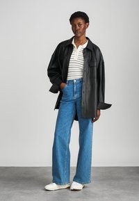 Juoda odinė perteklinė švarkelis, dėvimas ant baltos juostuotos polo marškinėlių, derinamas su aukštu liemeniu mėlynomis plačiomis džinsomis ir baltais sportbačiais.