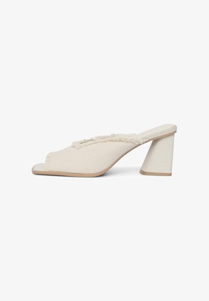 Mule in tela beige con punta aperta, dettagli con orlo sfilacciato e tacco a blocco alto e triangolare. Texture liscia con un design neutro.
