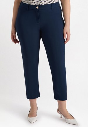 Pantaloni blu navy a vita alta con una texture liscia, tasca frontale e chiusura con bottone. Abbinati a tacchi bianchi a punta.