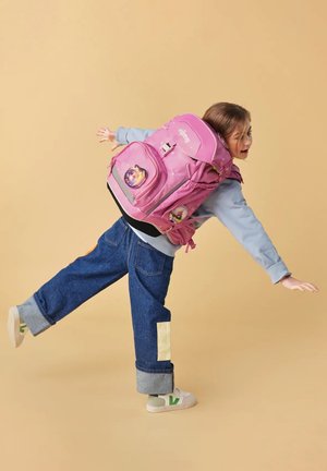 Pink backpack with character designs, multiple compartments, and adjustable straps. Blue jeans with cuffed hems and white sneakers with green accents.
