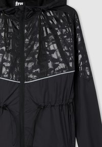 Czarna kurtka przeciwwiatrowa z błyszczącą, czarną wzorzystą górą, ściągaczem w talii oraz odblaskowymi detalami wzdłuż szwu klatki piersiowej.