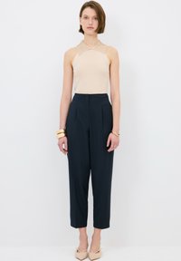Beige halter top s líme, v kombinaci s kalhotami s vysokým pasem v námořnické modři a béžovými lodičkami s špičatou špičkou. Zlatý náramek na zápěstí.
