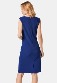 Blaues ärmelloses Kleid in taillierter Form mit einem Reißverschluss auf der Rückseite und einem Schlitz am Saum. Der strukturierte Stoff sorgt für visuelles Interesse.