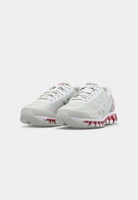 Baskets de sport blanches avec une tige en maille texturée, des accents rouges sur la semelle et un design de semelle rembourrée pour un soutien et un confort accrus.