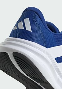 Modrá sportovní bota s texturovaným síťovaným svrškem, bílými akcenty a výraznou gumovou podrážkou s drážkami pro trakci.