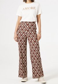 Spodnie o szerokich nogawkach w wyrazisty diamentowy wzór w kolorach czerwonym, białym i czarnym. Połączone z białym t-shirtem z napisem „AMORE”.